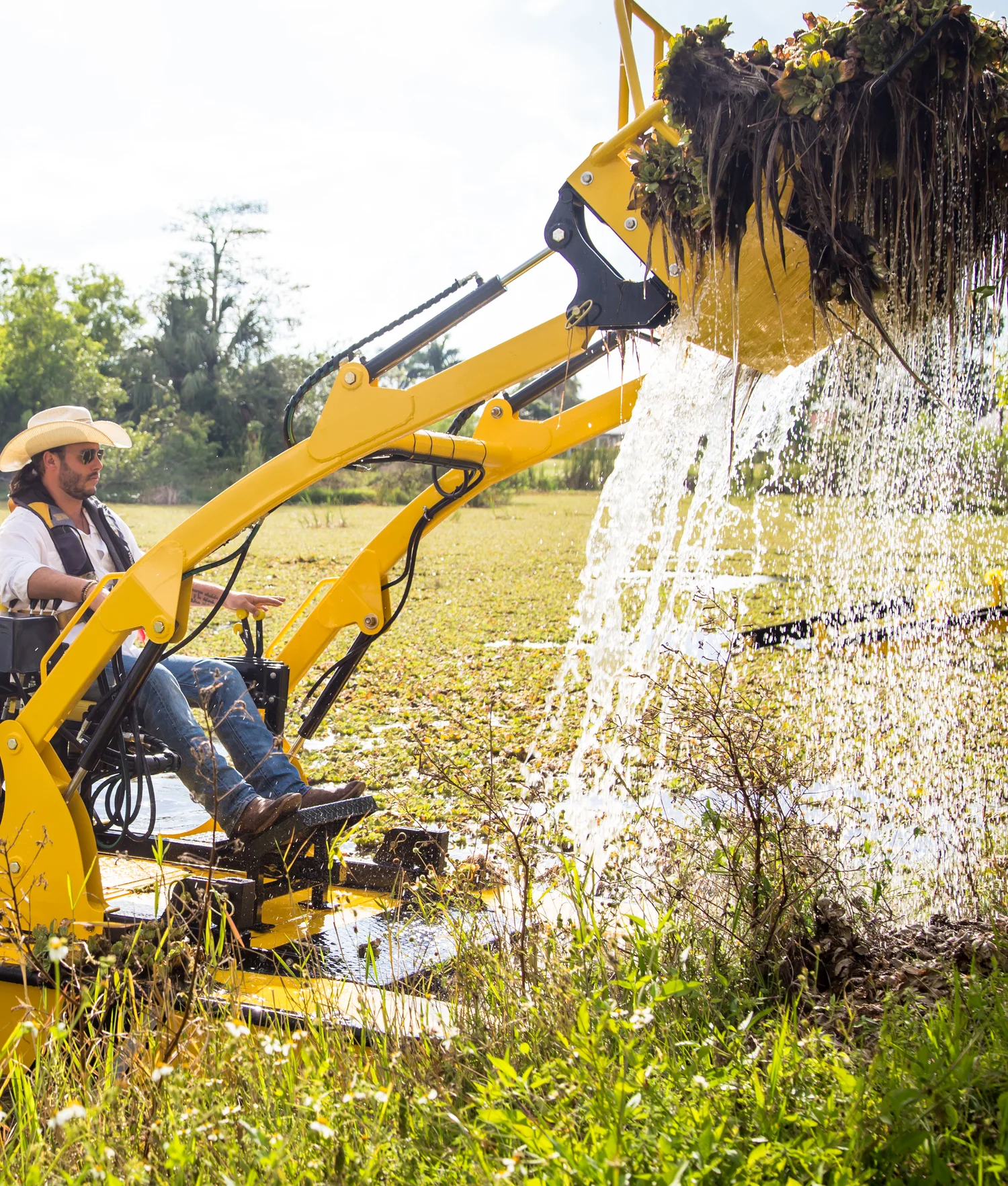 An operator lifting a dripping rake load of vegetation out of the water with a yellow Weedoo TC-3012 workboat